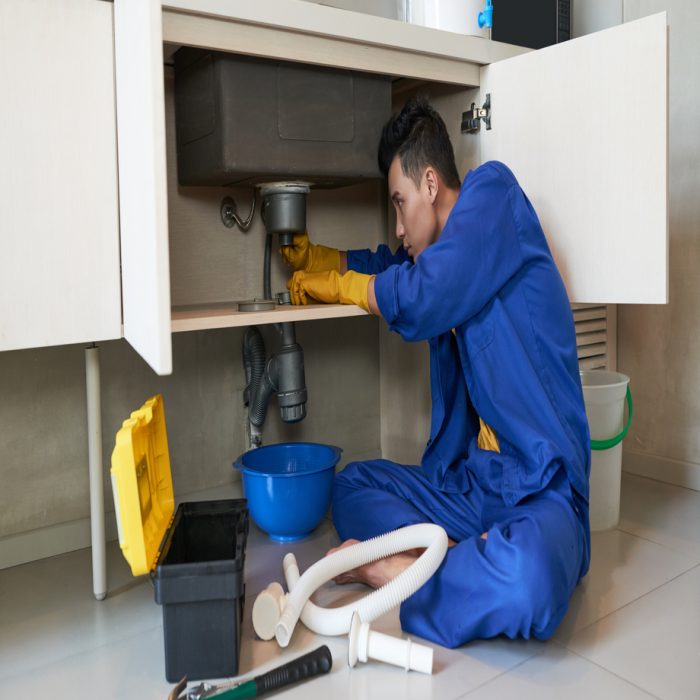 Young Vietnamese plumber checking drain in kitchen